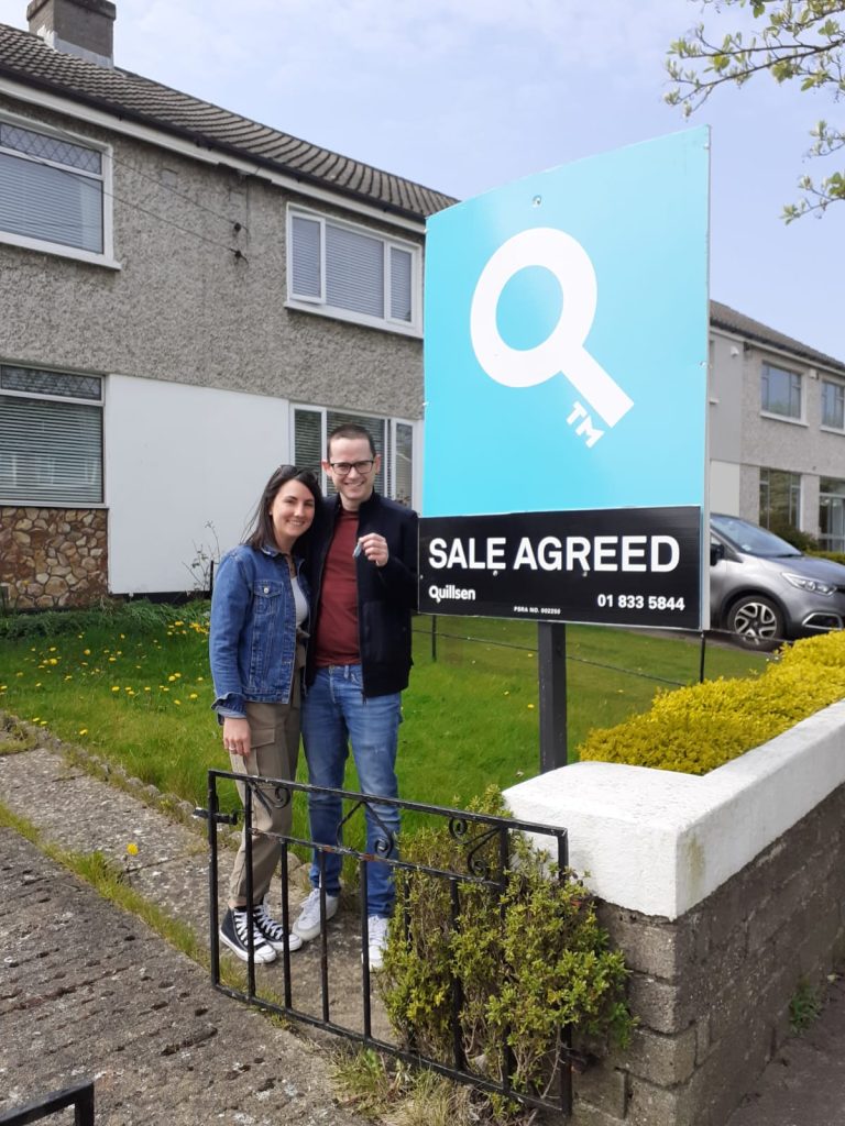 Couple standing by sale agreed sign outside house