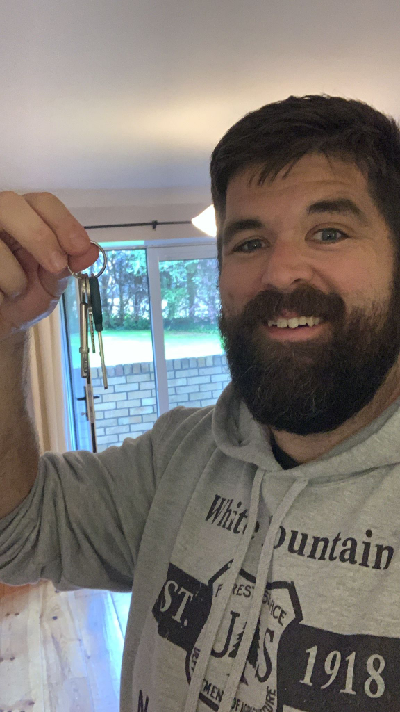 Man in hoodie smiling holding keys indoors